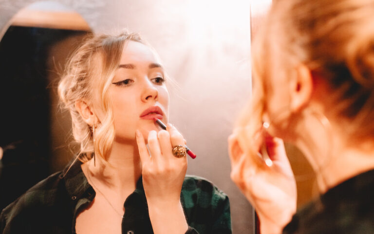 Young woman using lip pencil while drawing contours applying lipstick doing make up at home getting ready to go out
