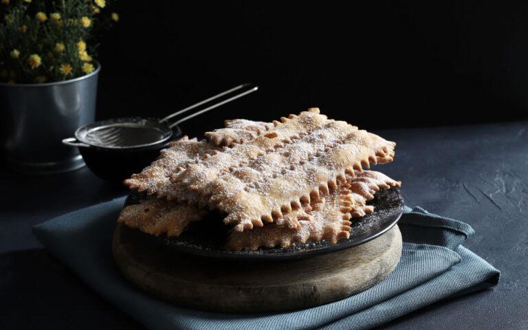 Carnival season. Homemade traditional Italian carnival sweets: chiacchiere sprinkled with icing sugar on dark background. Copy space. Overhead view.