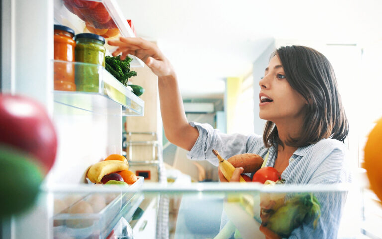 Closeup of a cheerful young couple picking some fruit and veggies from the fridge to make some healthy breakfast on Sunday morning. Shot from inside the working fridge.
