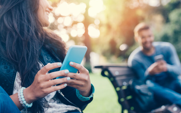 Happy couple using smartphones in the city park