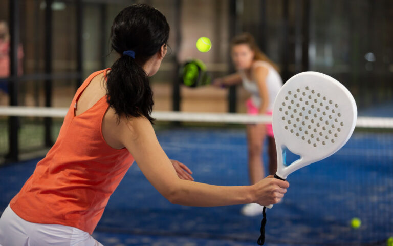 Rear view of brunette girl with white racket playing padel tennis at court
