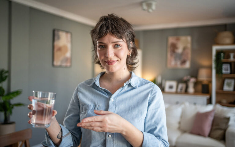 Young woman shows drinking glass with water, appeals for daily fluid intake