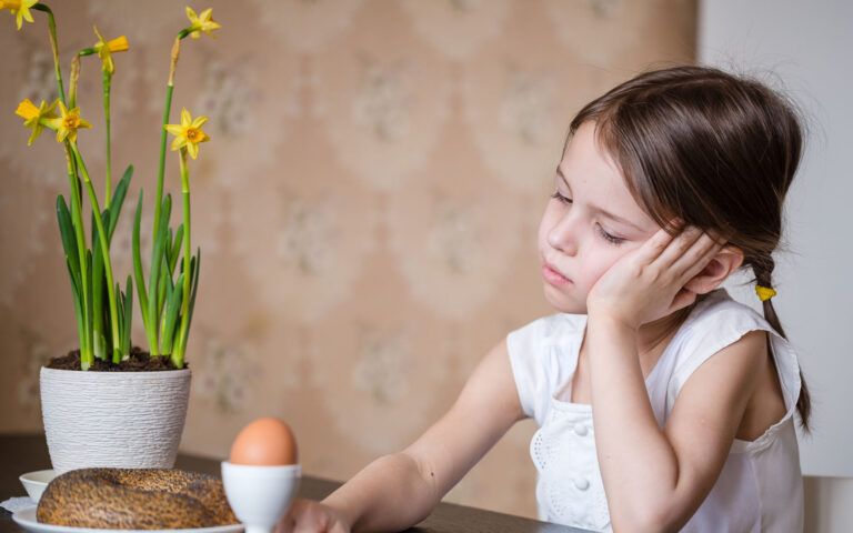 Thoughtful preschooler girl sitting at the table in the kitchen with pot flowers