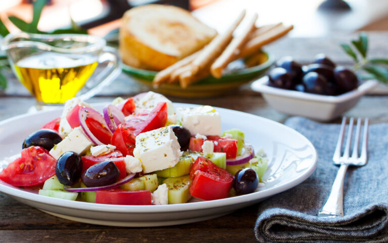 Greek salad. Fresh vegetables, feta cheese and black olives with white wine. Outdoor background.